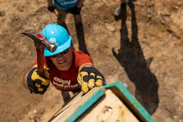 Person hammering nail into wood on build site.