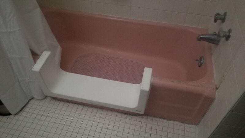 White tile in a bathroom, surrounding a pink bathtub. The middle of the side of the tub has been cut out, and replaced with a u-shaped white piece so you can step into the tub.