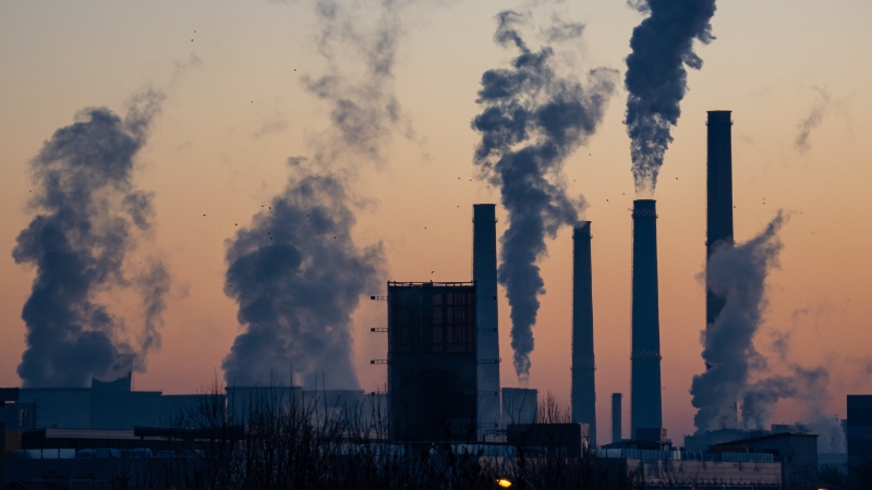 Different industrial plants with plumes of smoke and exhaust rising up.