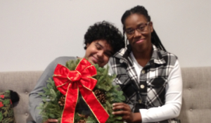 Homeowner Asia and her son sitting on a couch holding a holiday wreath and smiling