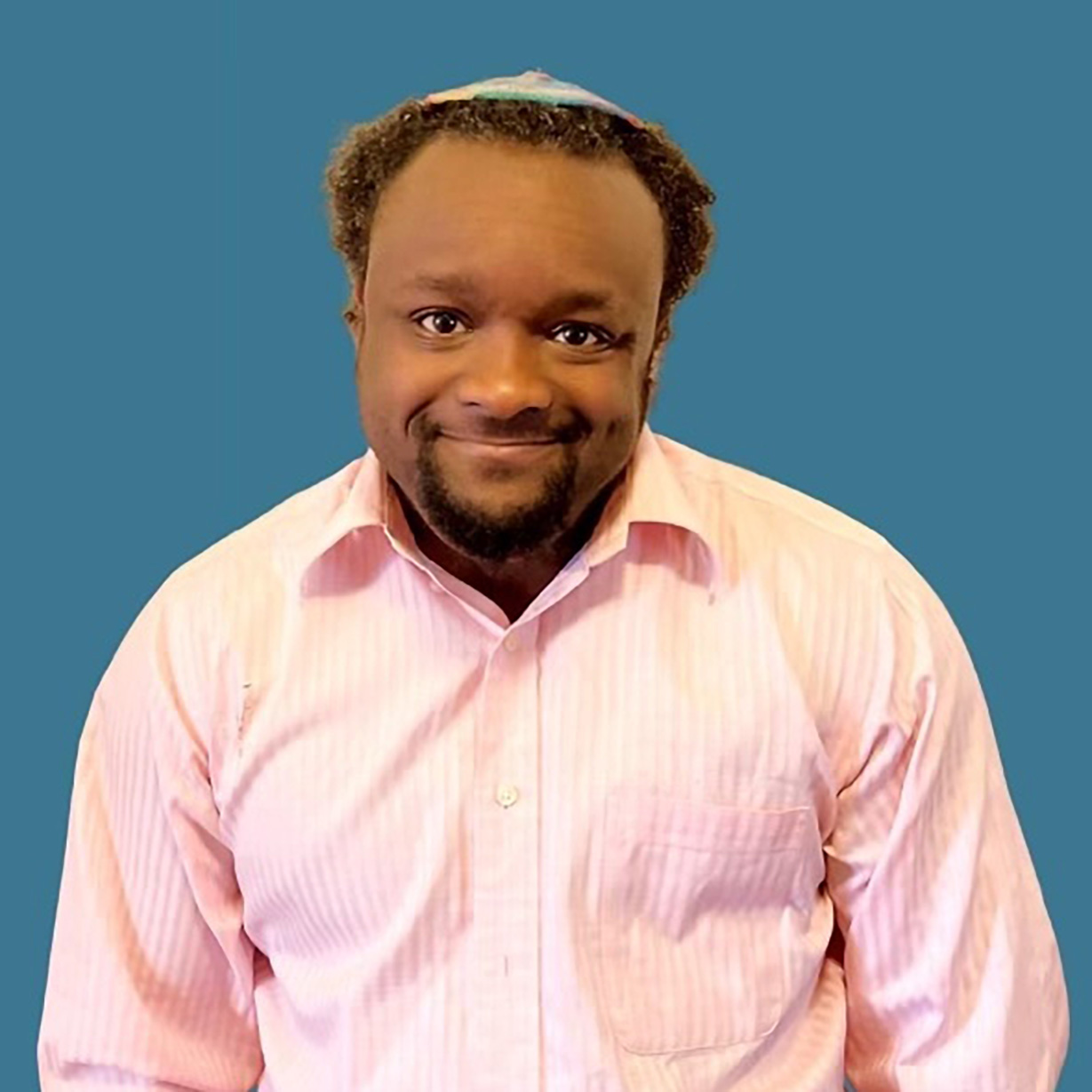 Profile picture of Enzi, a Black man, wearing a pink shirt and kippah.