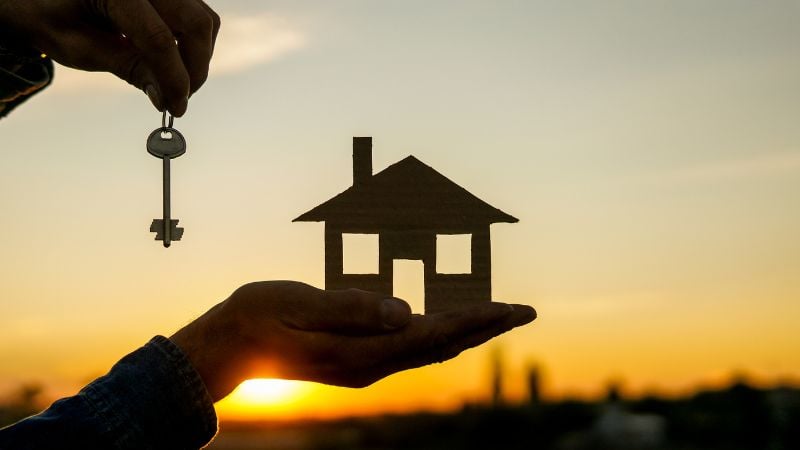 Silhouette of a key and a house in front of a sunset.