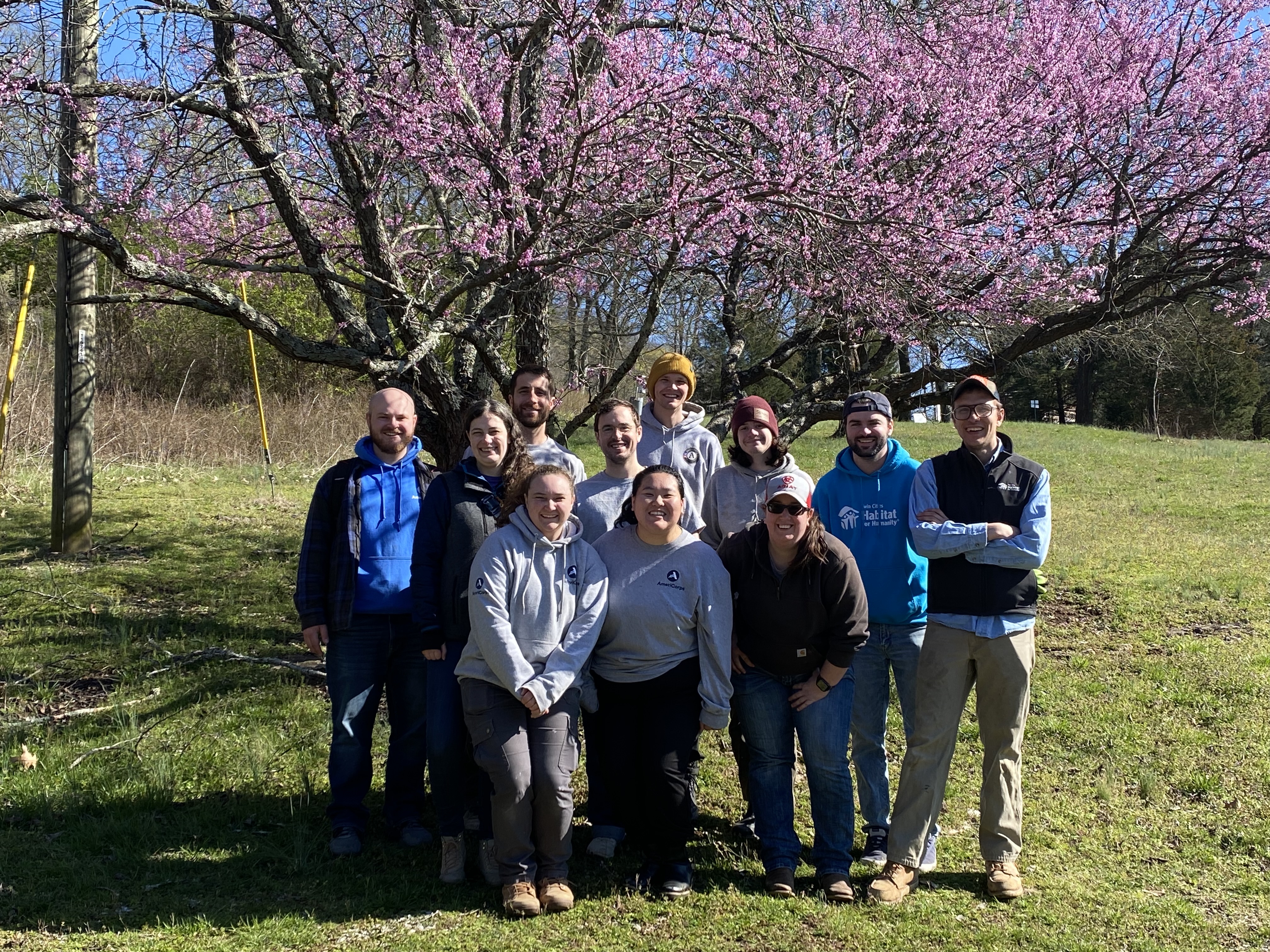 AmeriCorps Members pose in front of a flowering tree at the Owl's Hill Nature Sanctuary