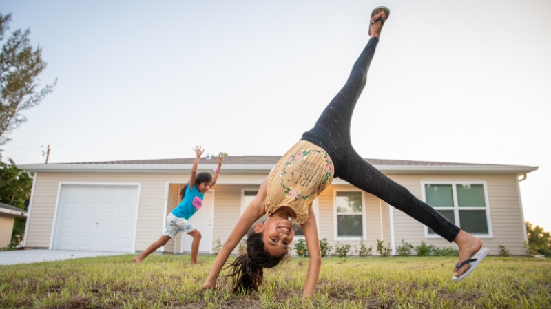 Two girls playing in the front yard of their house; one is mid-cartwheel.