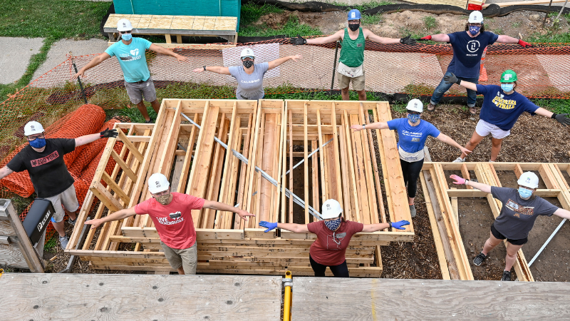 A group of socially-distanced people at a Habitat build site standing with their arms out