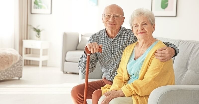 Elderly couple sitting together, male has his arm around female