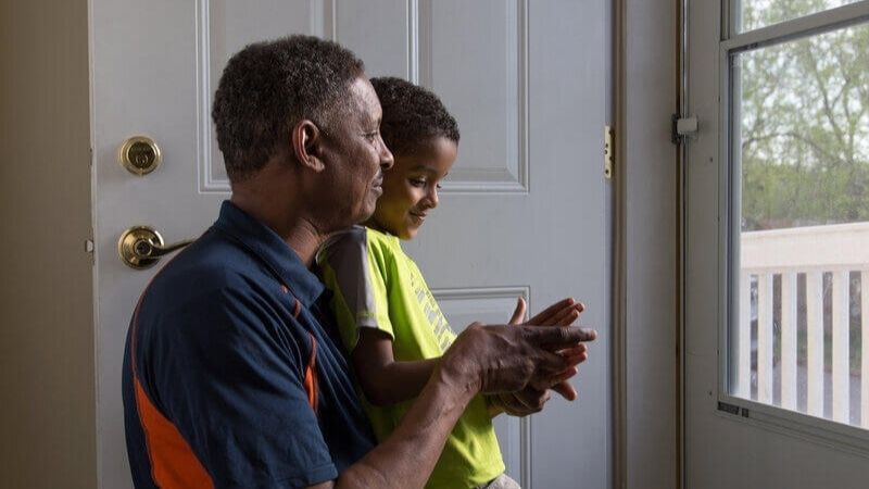 A Habitat homeowner sitting with his son, looking out their front door.