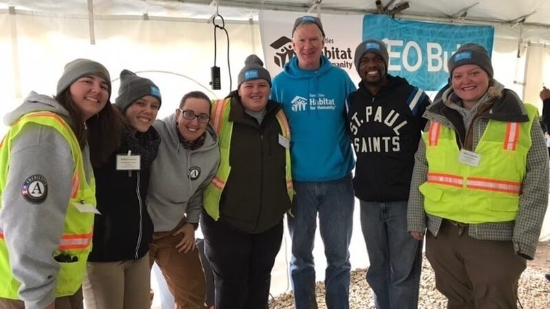 AmeriCorps members wearing Winter Warriors hats and posing with Chris Coleman at the CEO Build.