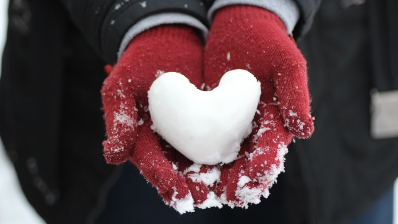 Heart-shaped snowball cradled in red gloves.