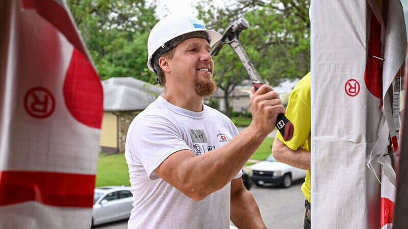 Corey smiling and hammering a door frame.