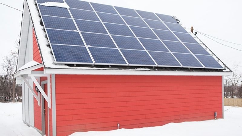 A bright red shed in the snow, with solar panels on the roof.