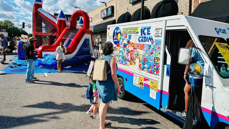 A family at an ice cream truck near an inflatable slide.